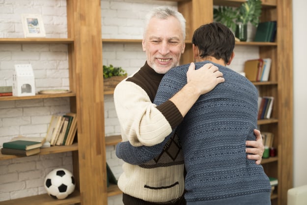 young-guy-hugging-with-aged-smiling-man-near-bookshelves