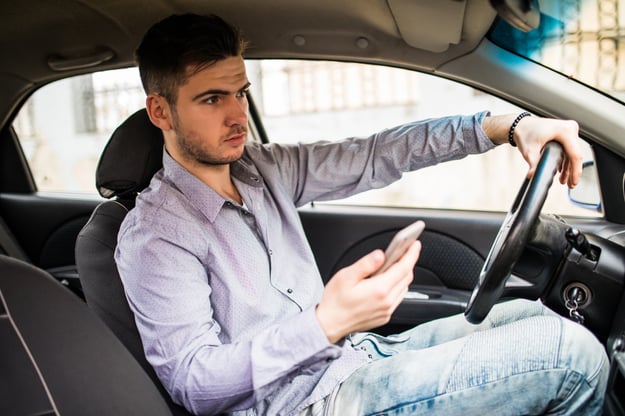 young-man-looking-mobile-phone-while-driving-car